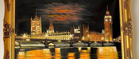 Un tableau encadré représentant une vue nocturne d’une ville, avec ses bâtiments emblématiques et un pont.