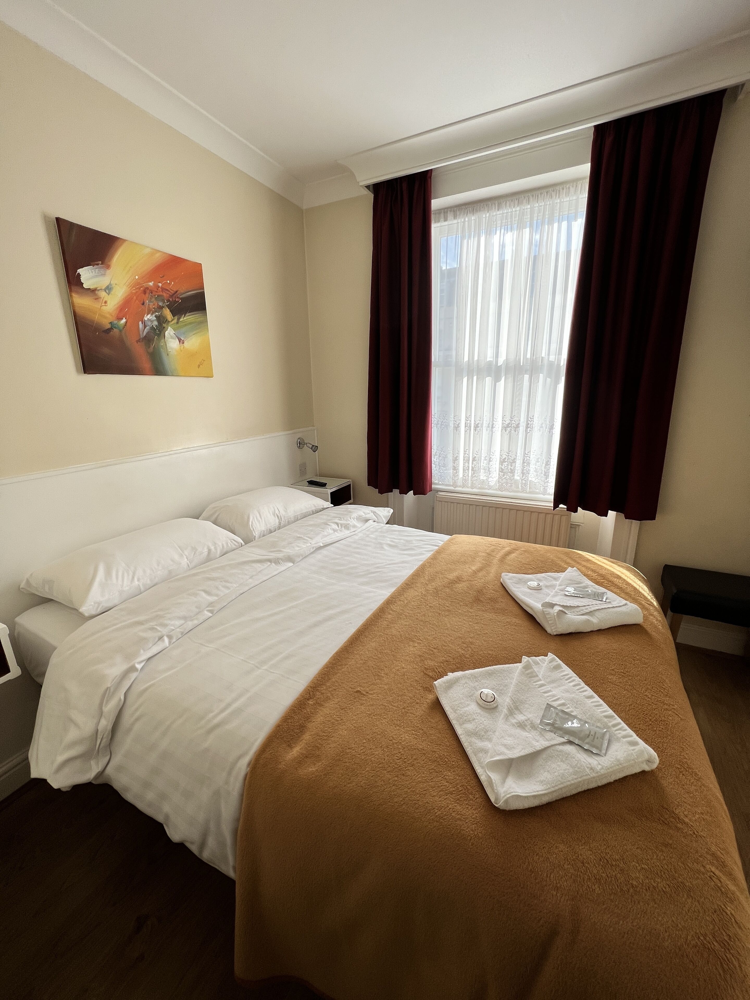 Une chambre d’hôtel avec un grand lit, une table de chevet, un tableau au mur et une fenêtre avec des rideaux.