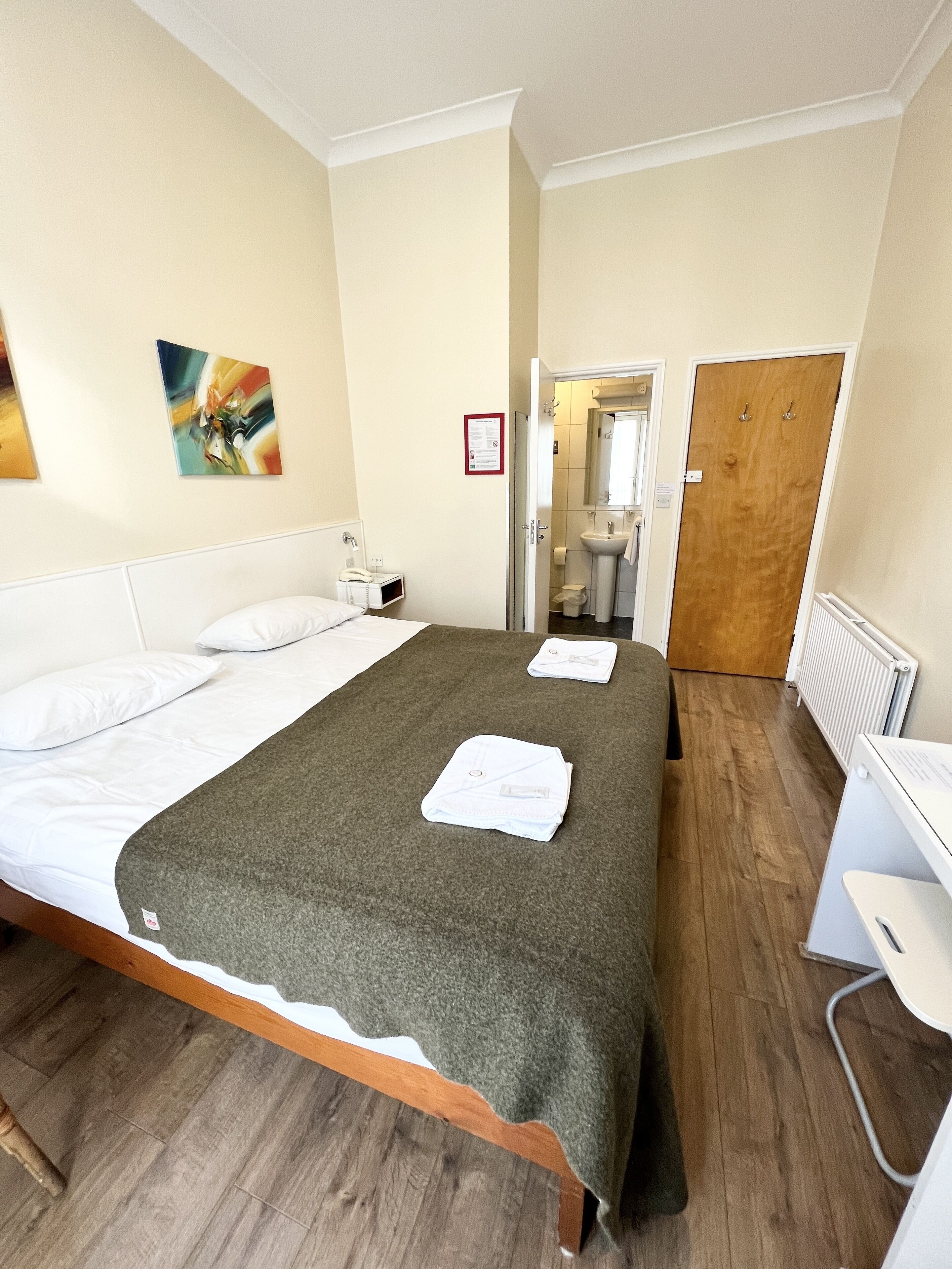 Een hotelkamer met een bed, een bureau, een stoel, een badkamer en een deur.