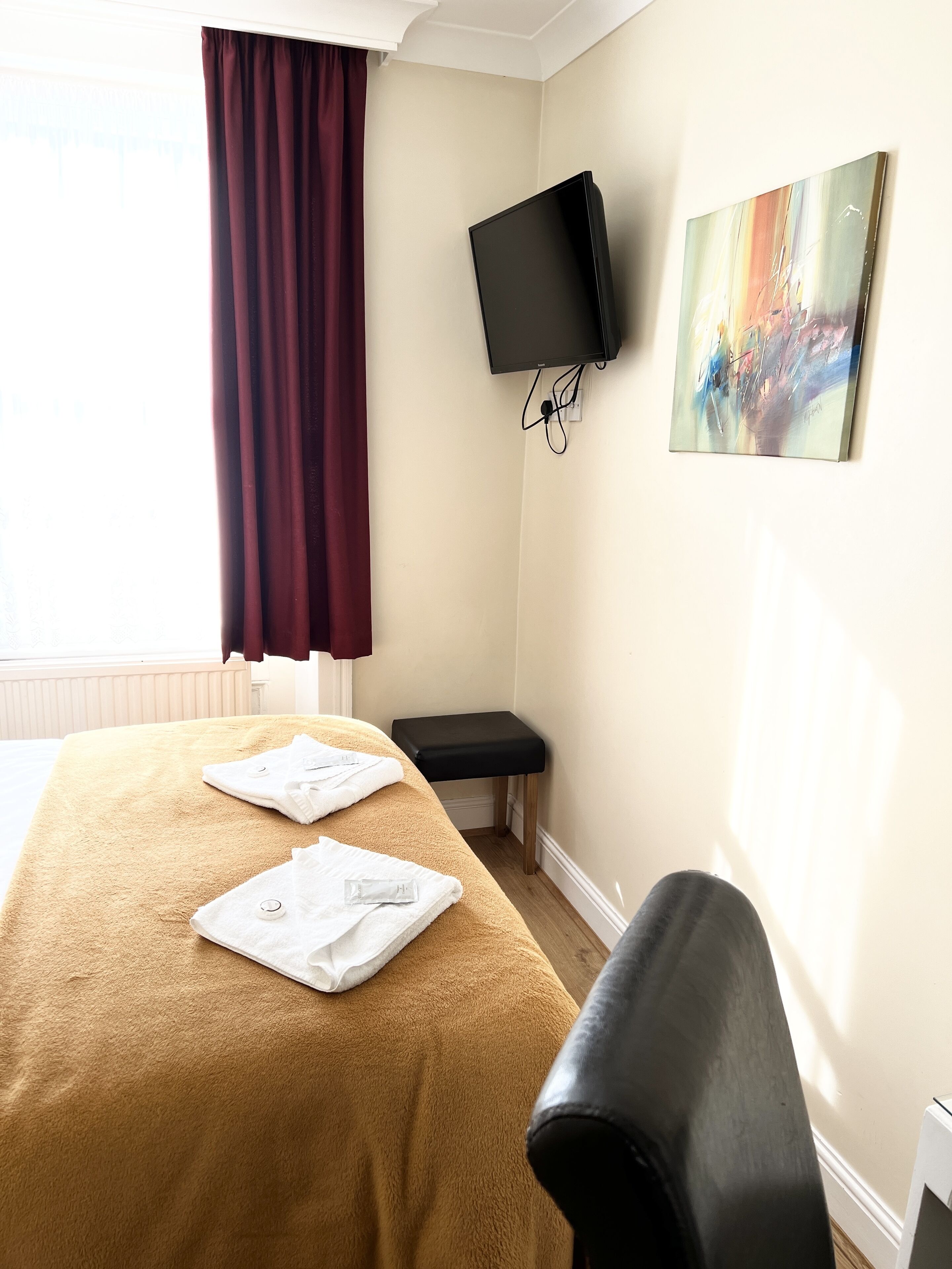 A hotel room with a bed, a TV mounted on the wall, a painting, and a window with curtains.