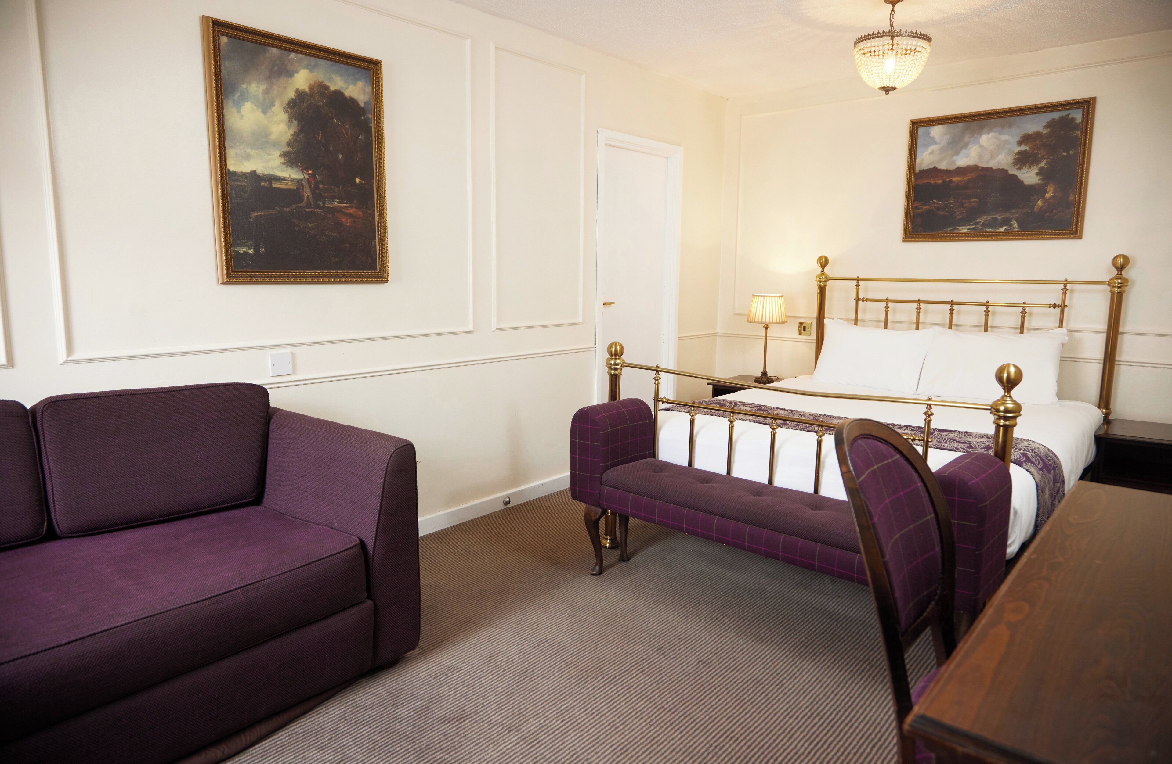 Quarto de hotel com cama, sofá, poltrona e duas pinturas nas paredes.