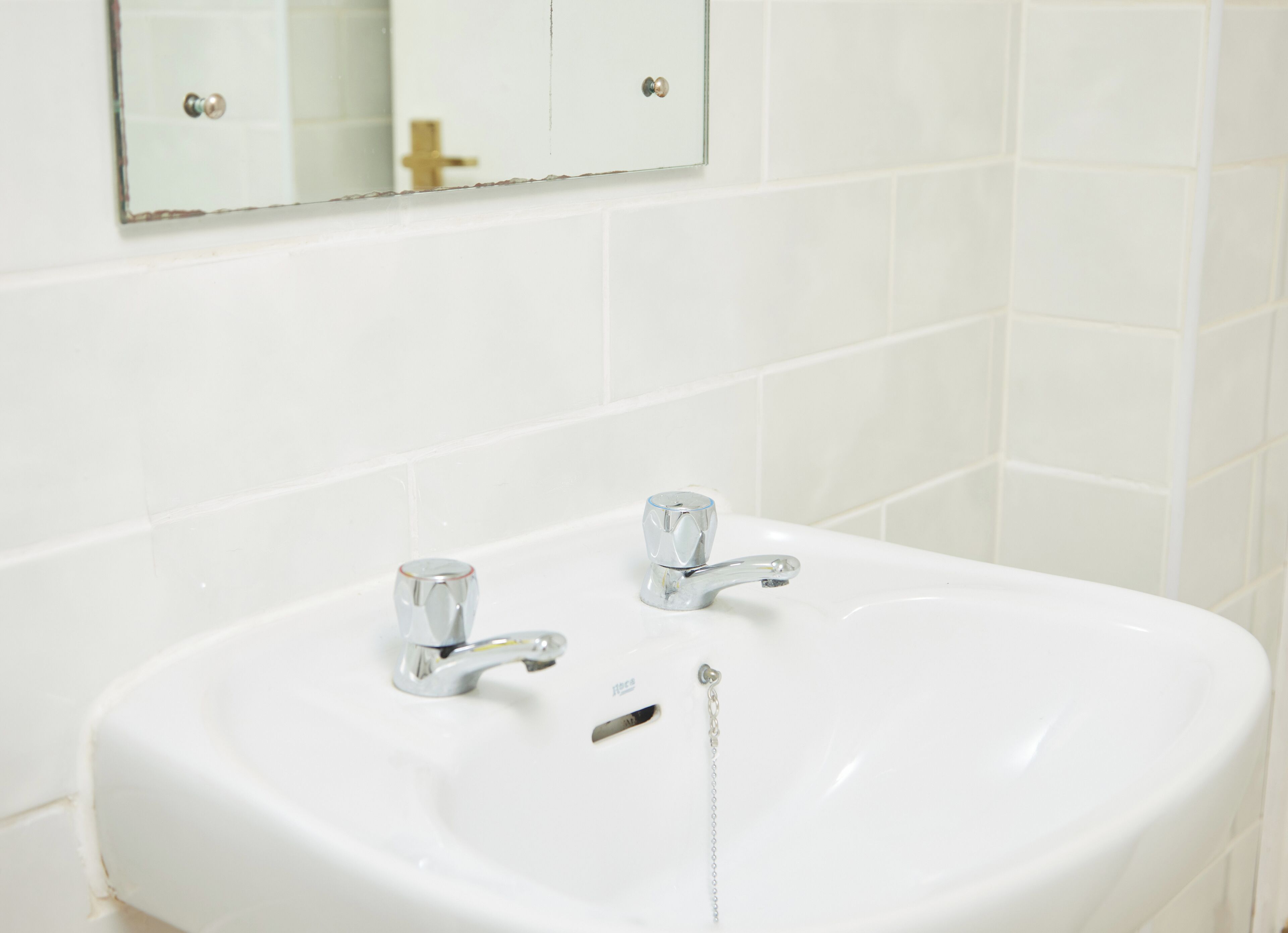 A white bathroom sink with two faucets and a mirror above it.