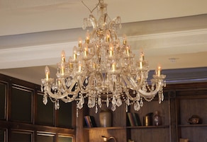 Un candelabro con múltiples luces y adornos de cristal en una habitación con paneles de madera y estanterías.