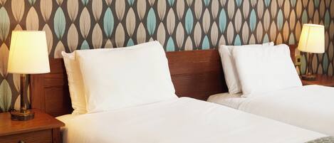 Habitación de hotel con dos camas, cabeceros de madera y mesitas de noche con lámparas.