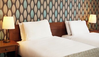 Habitación de hotel con dos camas, cabeceros de madera y mesitas de noche con lámparas.