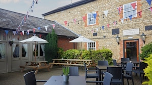 An outdoor seating area with tables and chairs, a wooden picnic table, and a sign for "The Coach House". - Cock Hotel Stony Stratford by Greene King Inns (Milton Keynes)