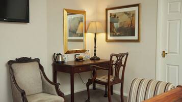 Een hotelkamer met een houten bureau, twee stoelen, een lamp, een televisie en een deur.
