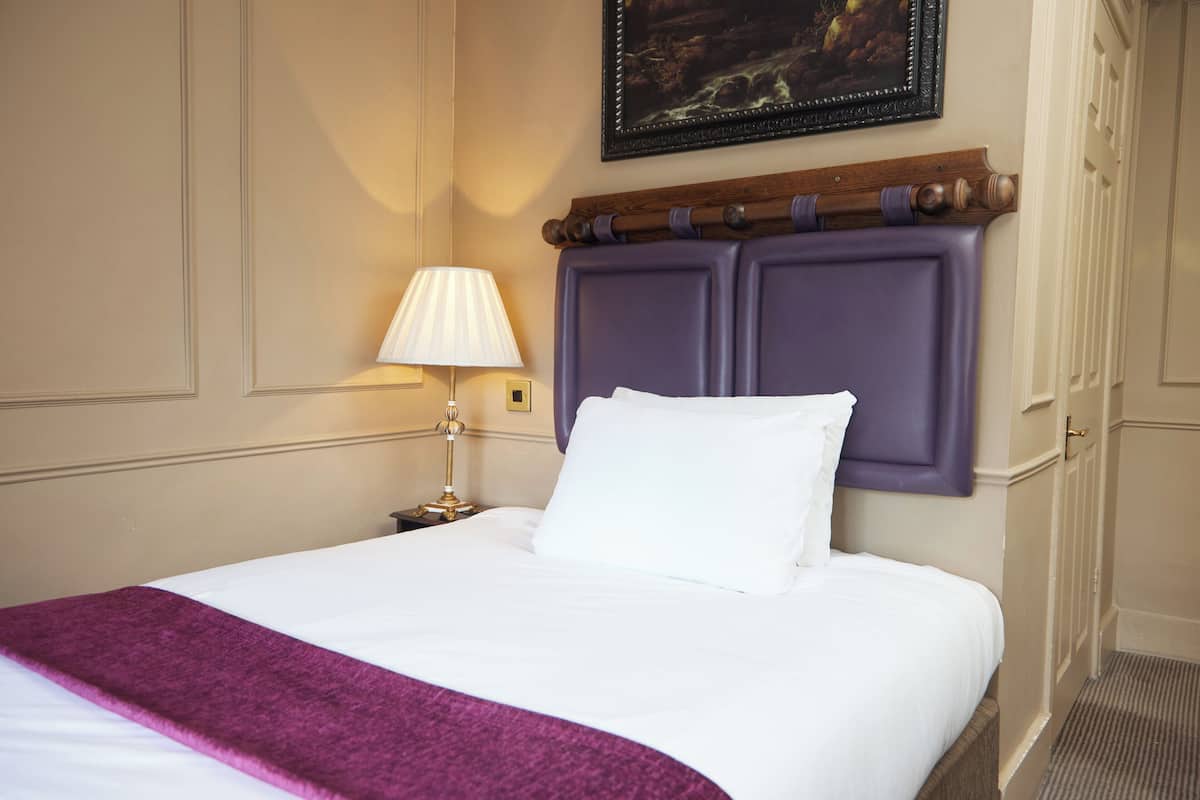 A neatly made bed with a purple headboard, a white pillow, and a purple throw blanket.