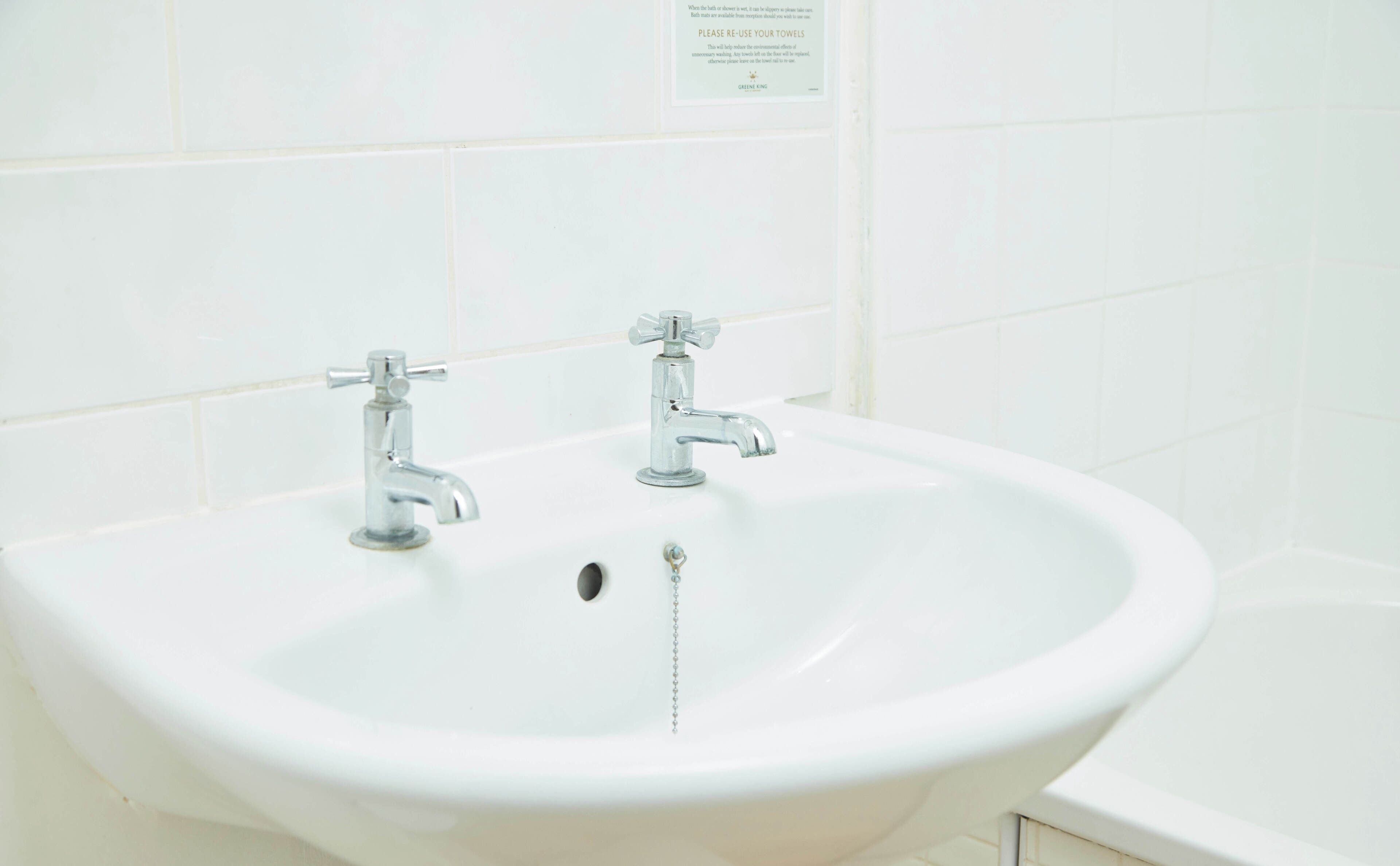 A white bathroom sink with two faucets and a drain.