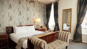 A neatly arranged bedroom with a large bed, a bedside table, a lamp, a chair, a mirror, and a window with curtains. - Cock Hotel Stony Stratford by Greene King Inns (Milton Keynes)