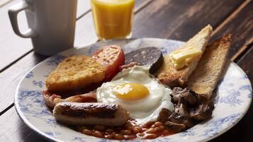 Une assiette de nourriture pour le petit-déjeuner comprenant des œufs, des saucisses, des haricots, des toasts et une tranche de tomate.