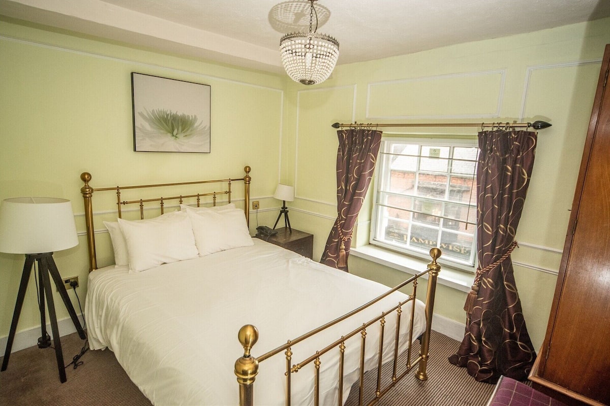 A room with a bed, a lamp, a window with curtains, and a chandelier.