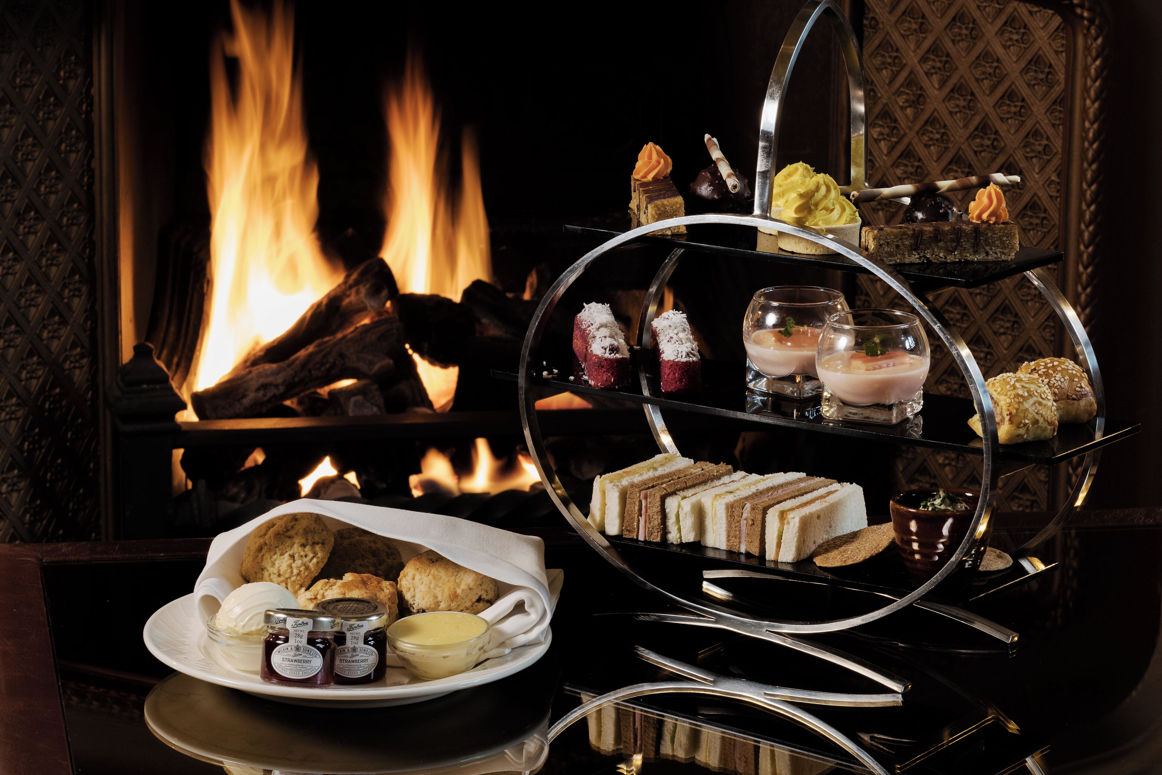 A dessert display with various sweets and pastries, a plate with biscuits and butter, and a glass of milk.