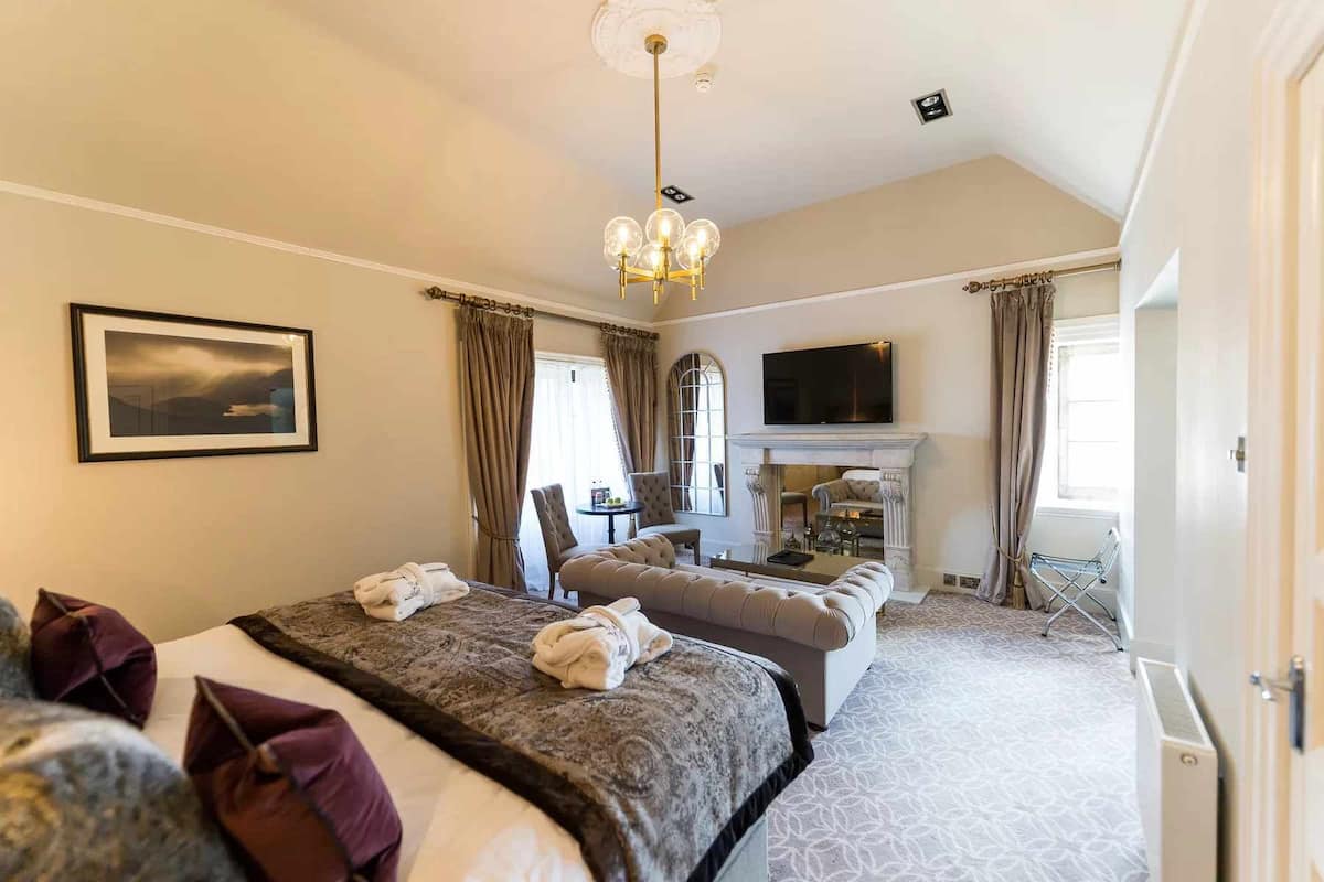 A spacious hotel room with a large bed, a sofa, a TV, and a fireplace.