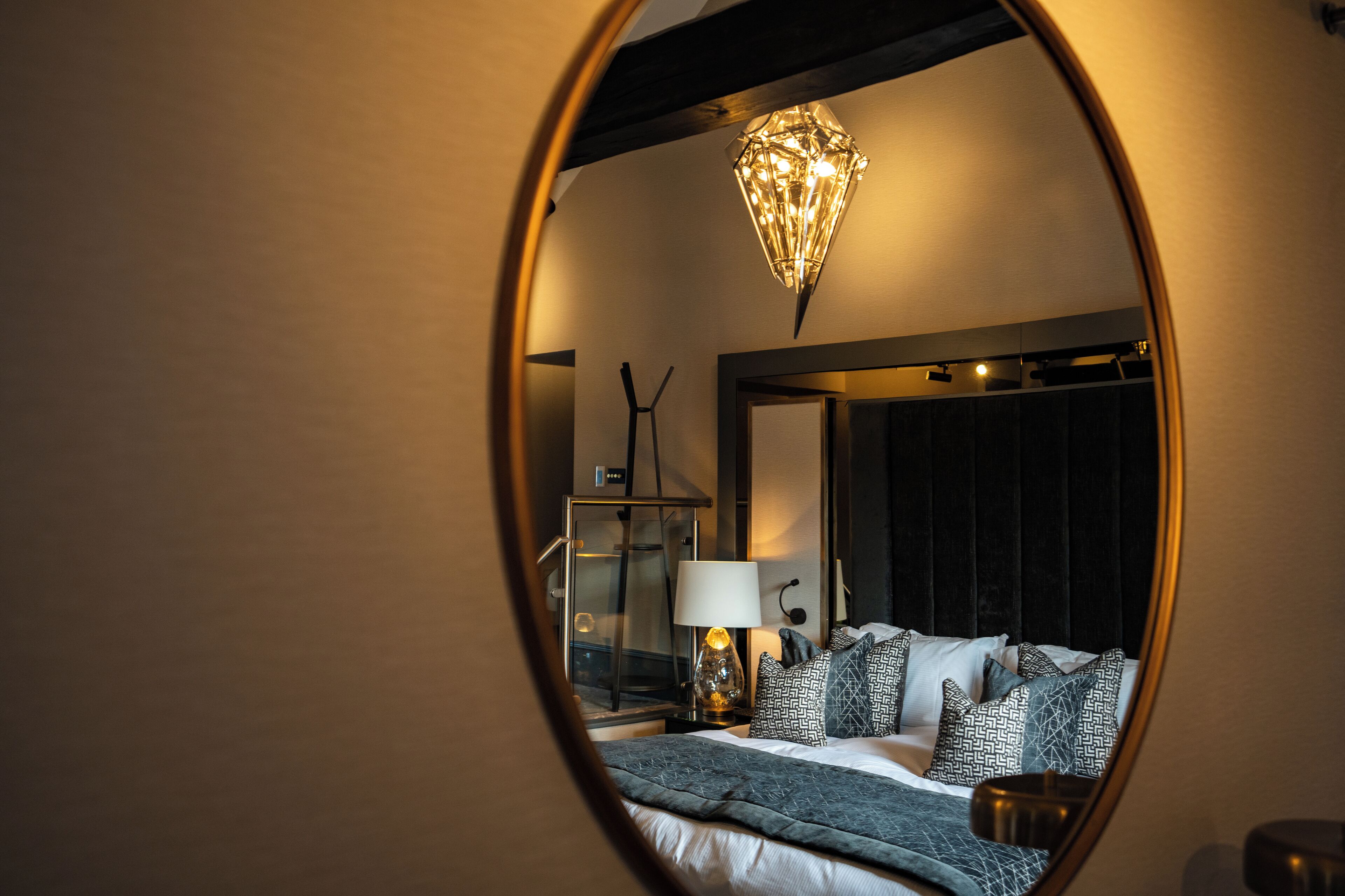 Quarto com cama, mesa de cabeceira com abajur, espelho e luminária pendente.