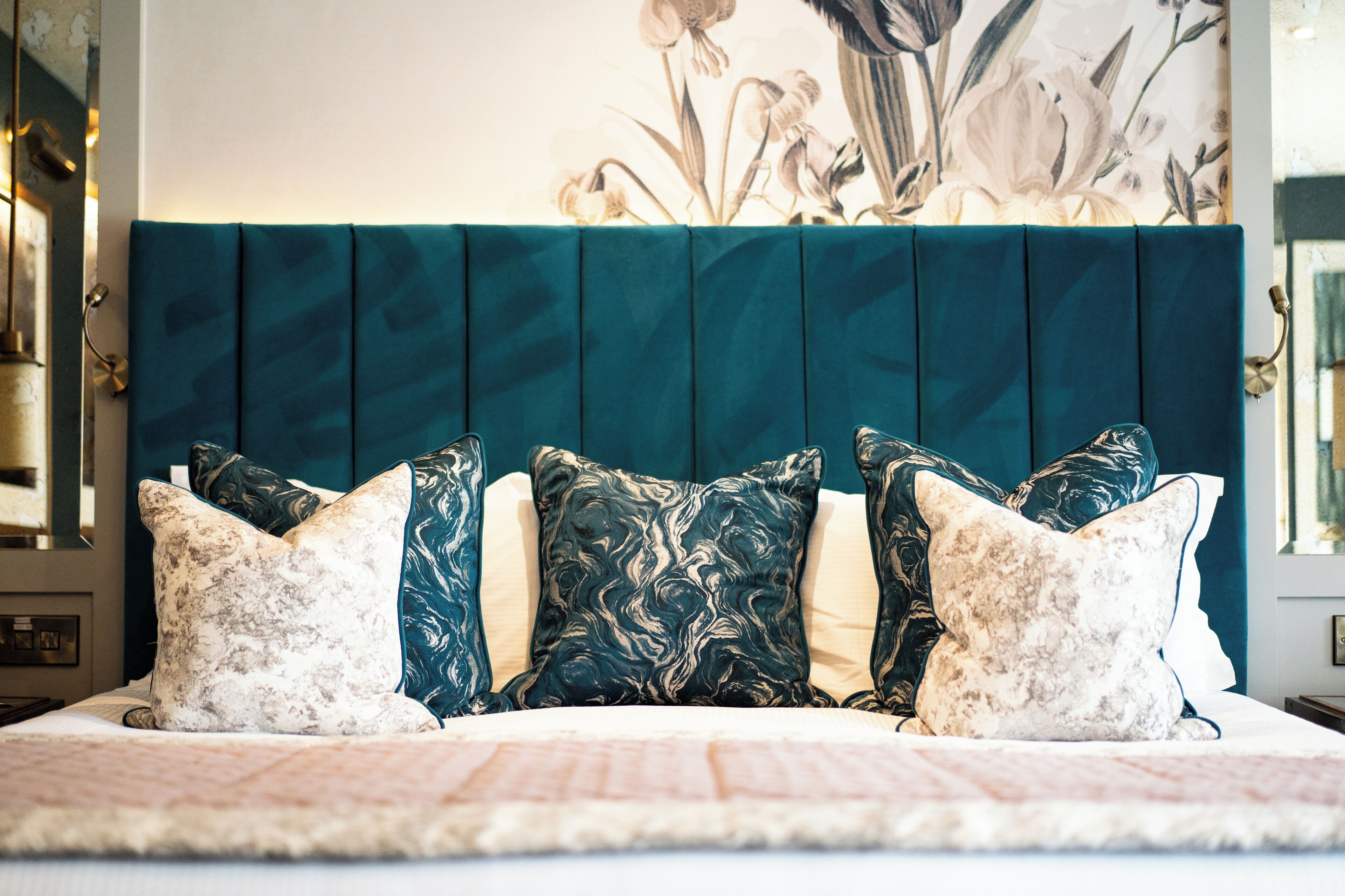 A bed with a teal headboard, multiple pillows, and a floral wall mural.
