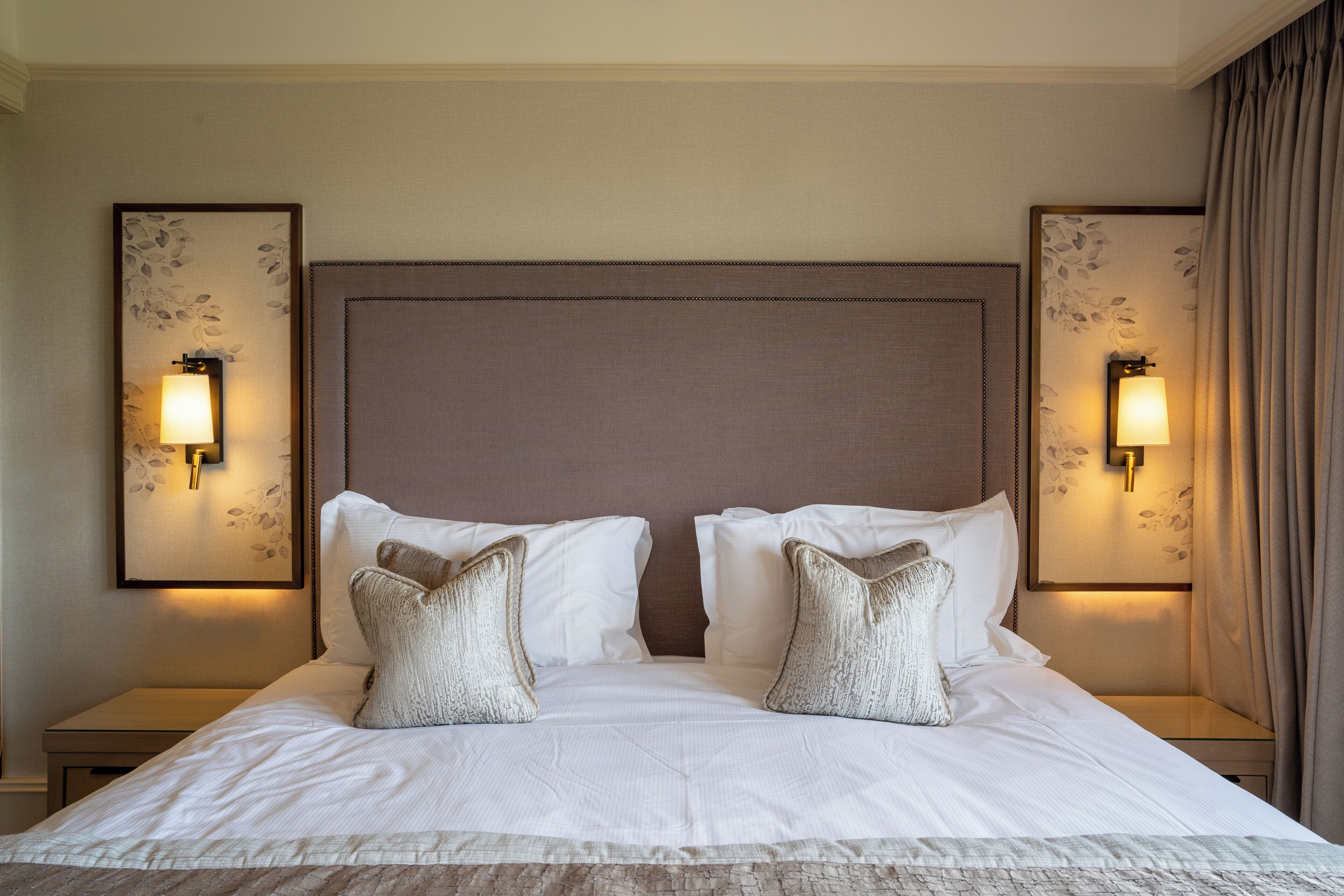 A hotel room with a large bed, two bedside tables, and wall-mounted lamps.