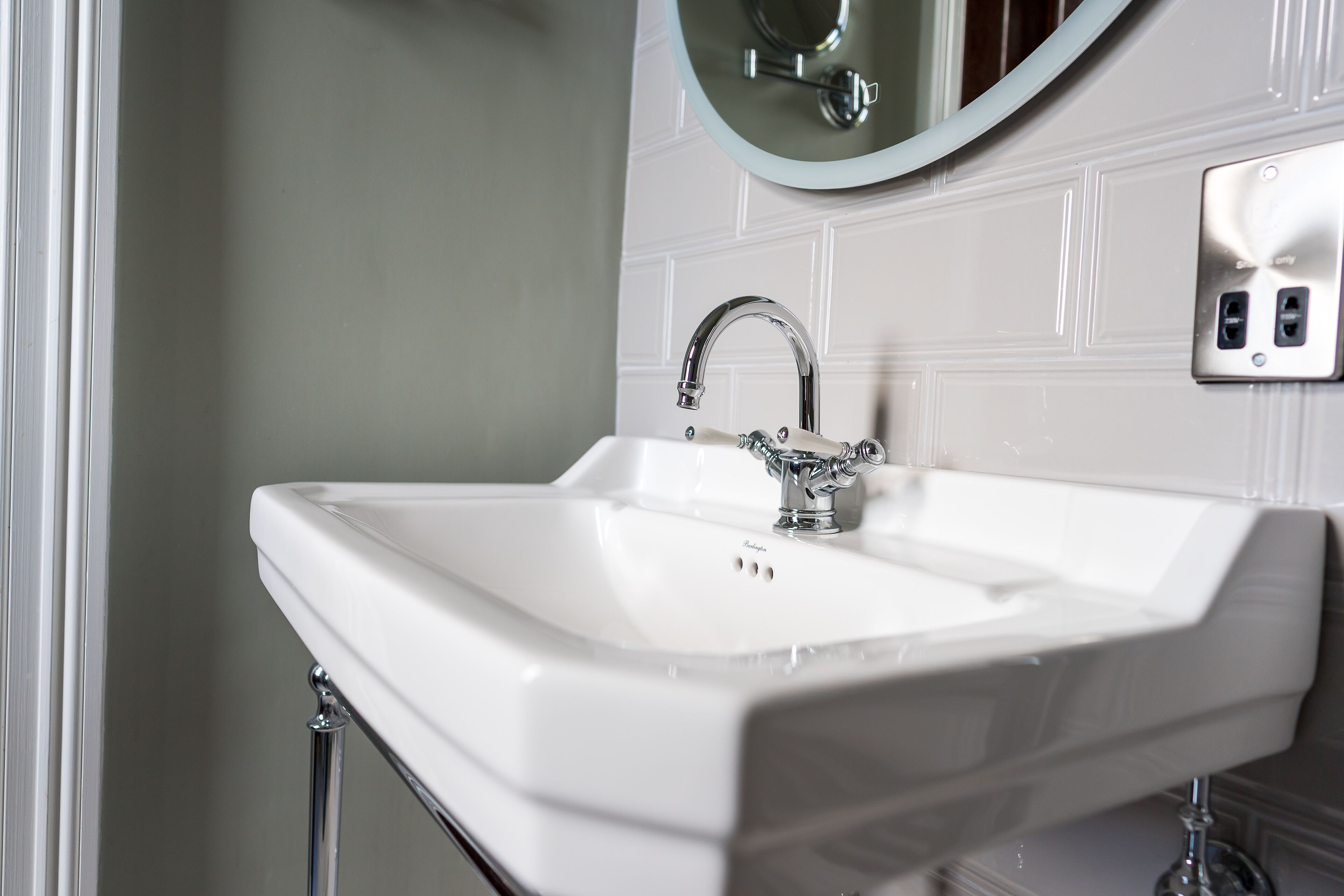 A white bathroom sink with a chrome faucet, a mirror above it, and a wall-mounted electrical outlet.