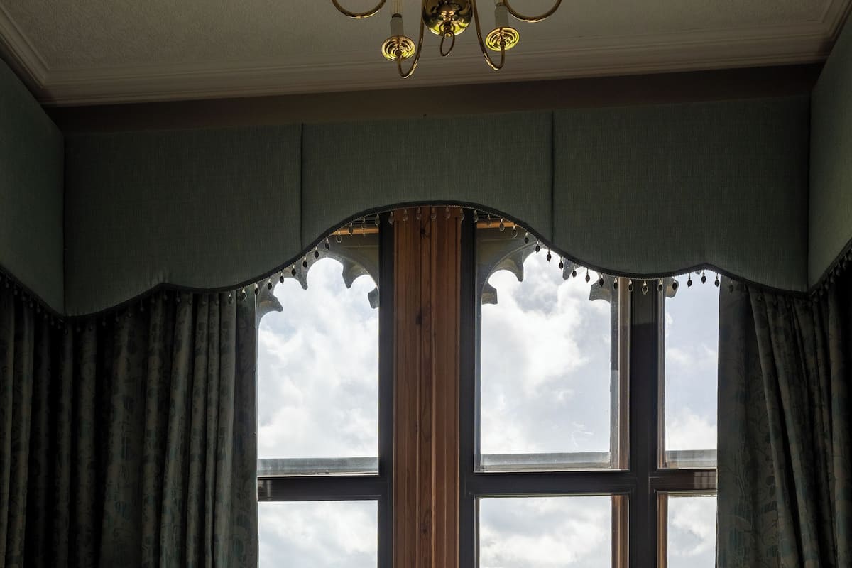 A room with two upholstered armchairs, a round table with a lamp, and a view of mountains through large windows.