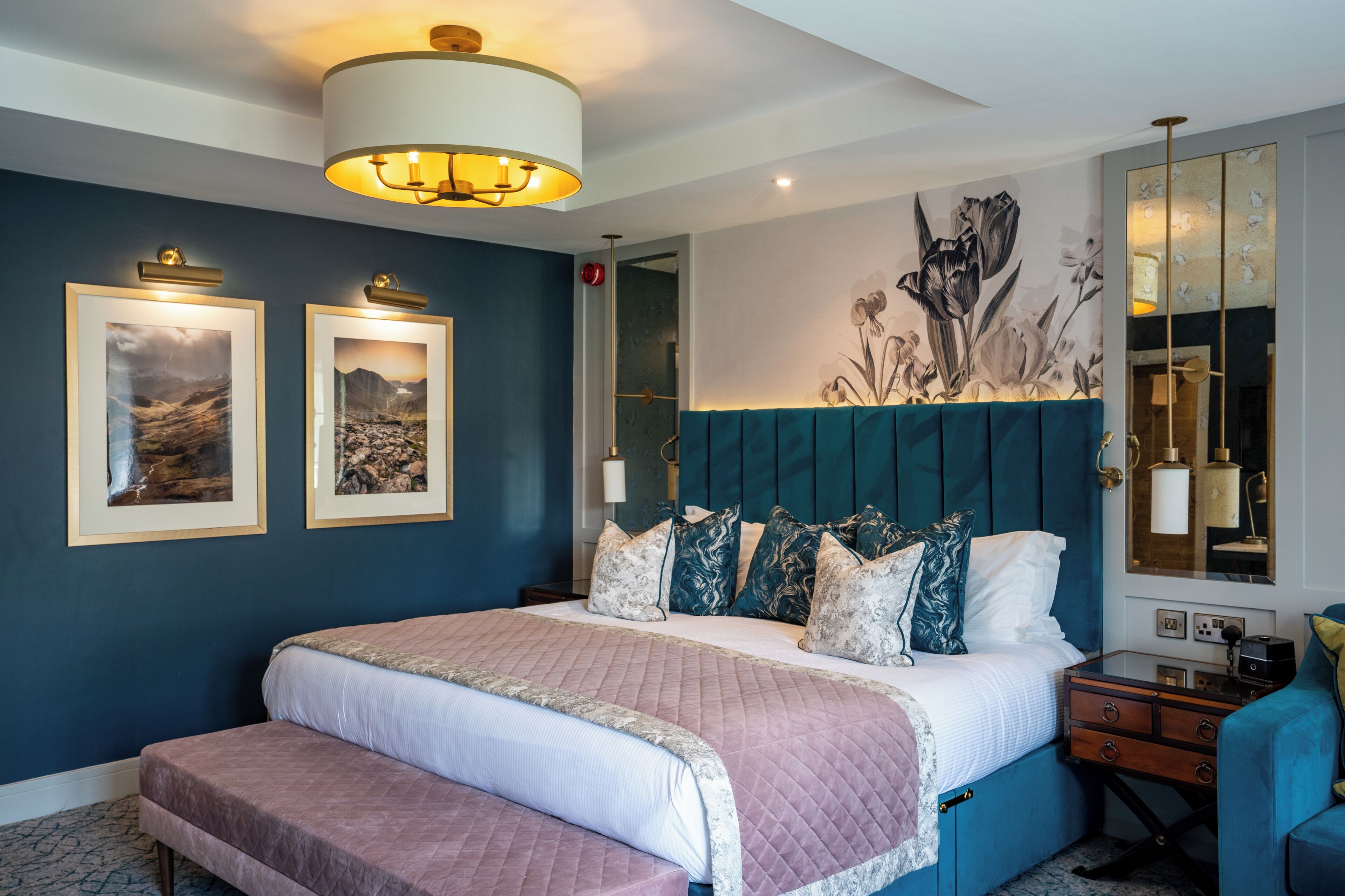 Un dormitorio con una cama grande, un banco, una mesita de noche, un espejo y decoración en la pared.