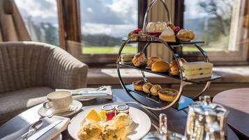 A three-tiered dessert stand with various pastries and sandwiches, a cup of tea, and a table setting with cutlery and condiments.