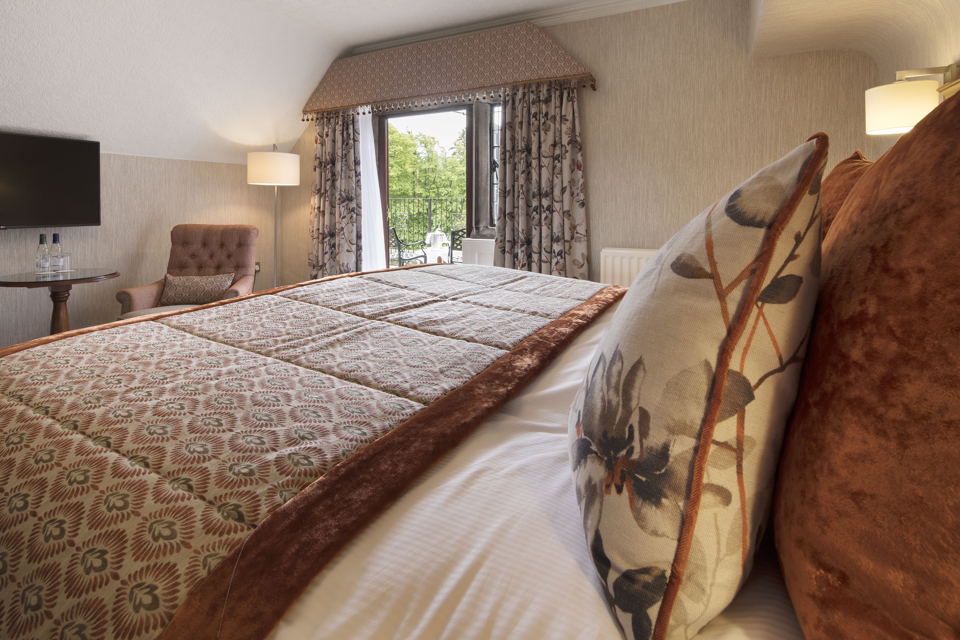 A hotel room with a large bed, a chair, a TV, and a view of the outdoors.