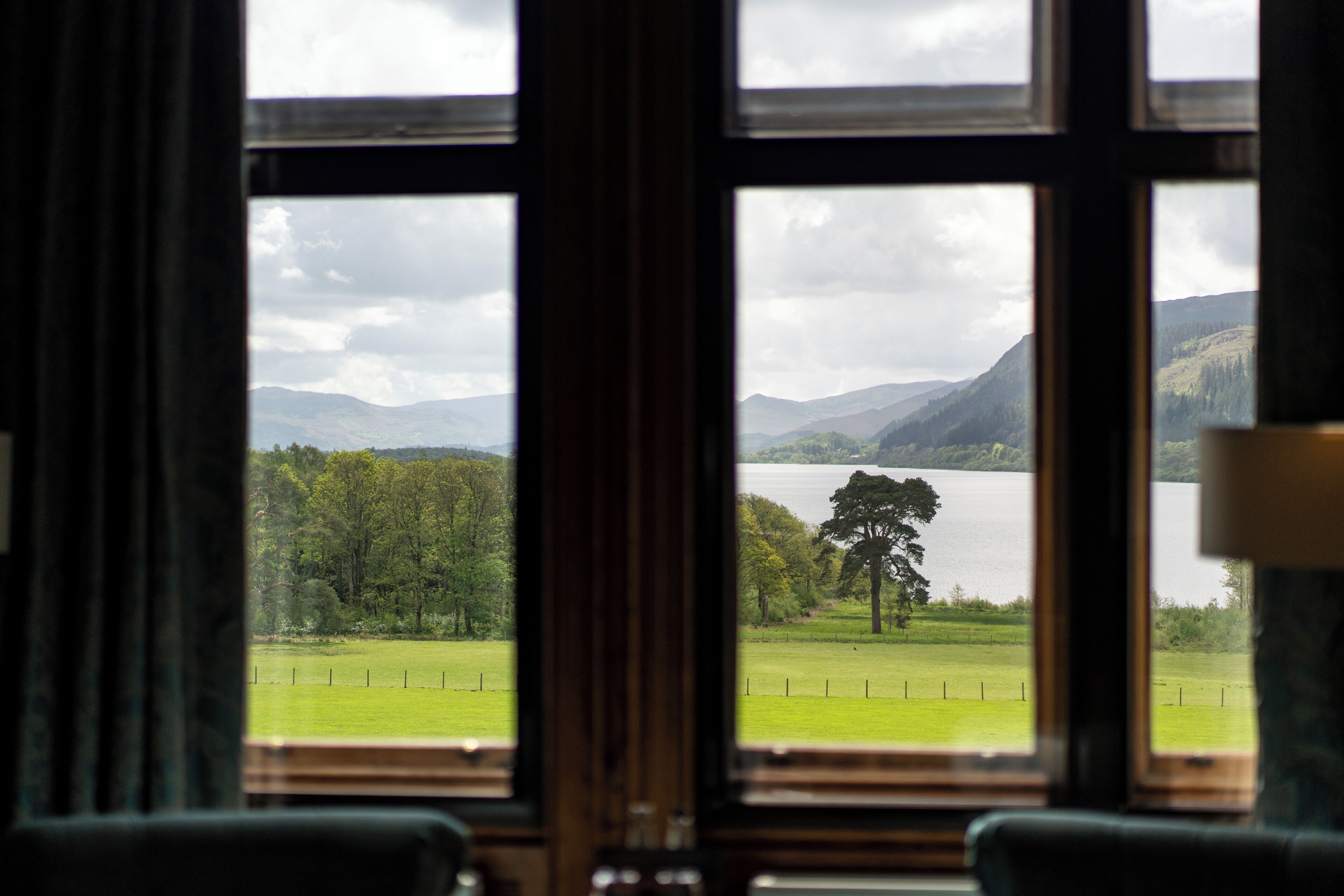 A view through a window with a landscape of a lake, trees, and mountains.