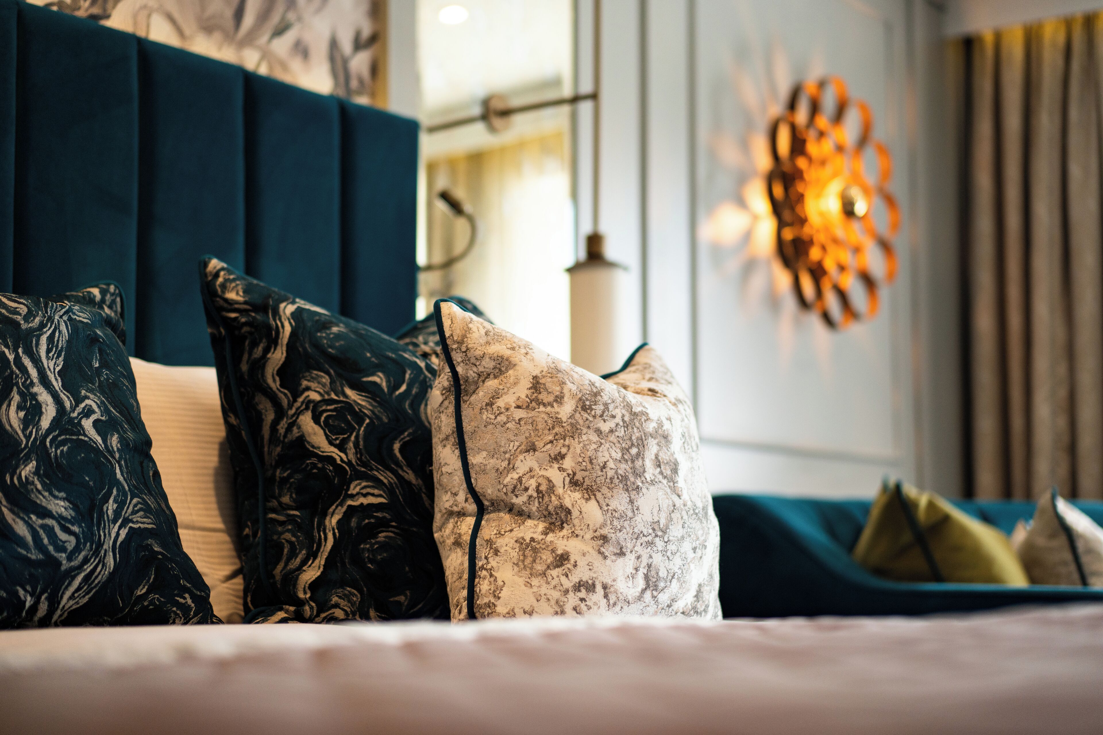 Ein Bett mit vielen Kissen, einem blauen Kopfteil und einer Wandleuchte.