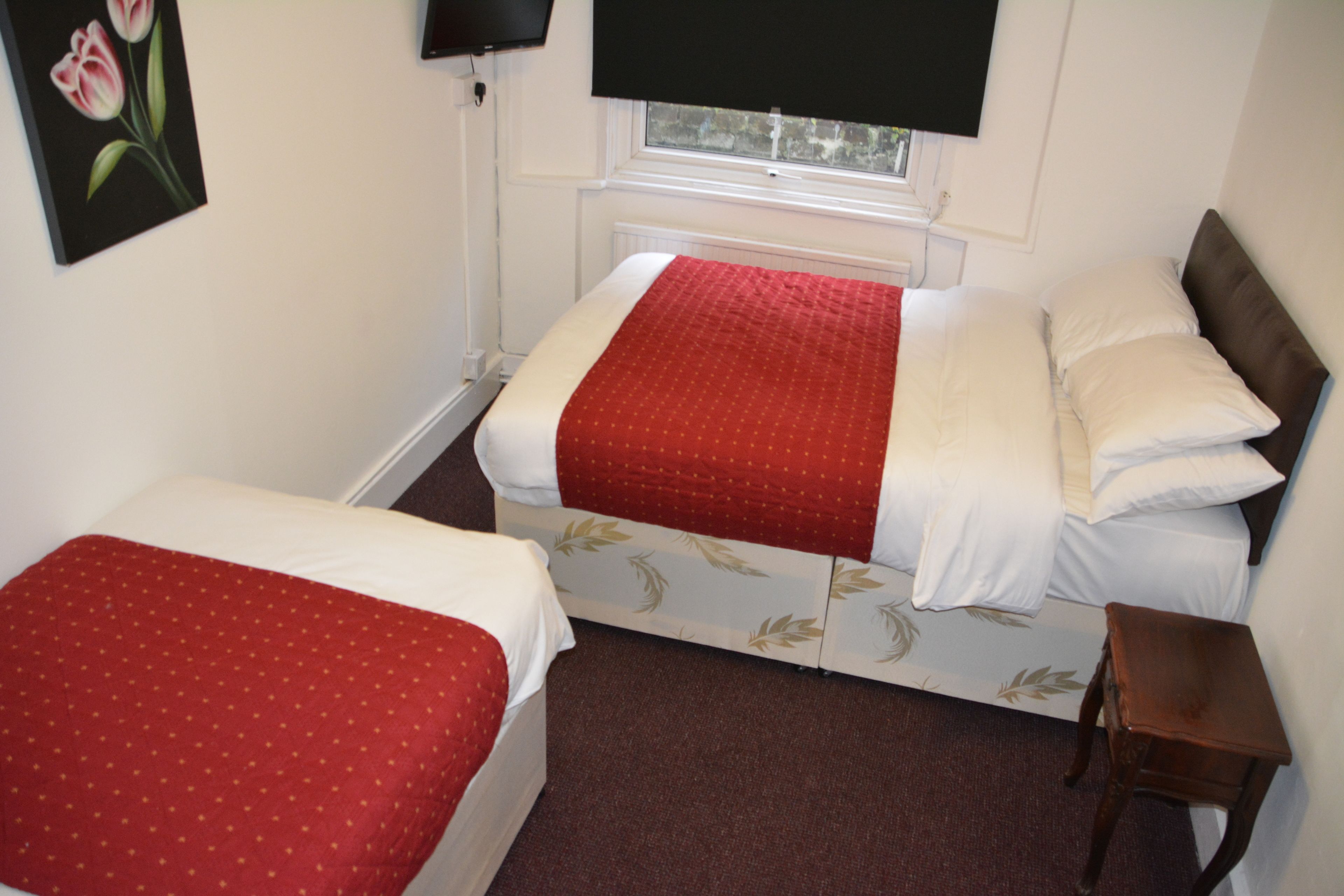 A room with two beds, each with a red and white bedspread, a small wooden nightstand, and a painting of a tulip on the wall.