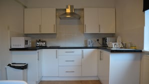 A compact kitchen with white cabinets, a microwave, a toaster, and a kettle. - Bow Guest House (Reading)
