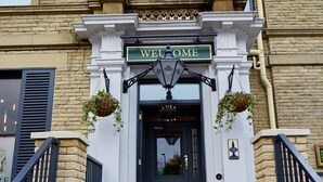 A building with a "WELCOME" sign above the entrance, stone steps leading up to the door, and hanging planters on either side. - Belmore (Sale)