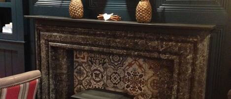 A room with a dark blue wall, a fireplace with a patterned mantle, and a small table with candles.