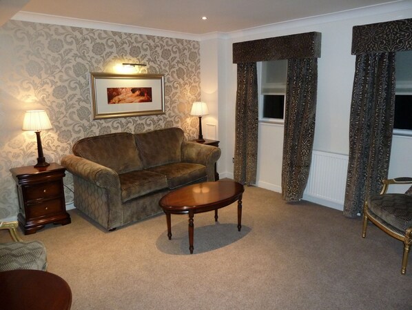 A living room with a patterned sofa, two side tables with lamps, a small round table, and a window with curtains.