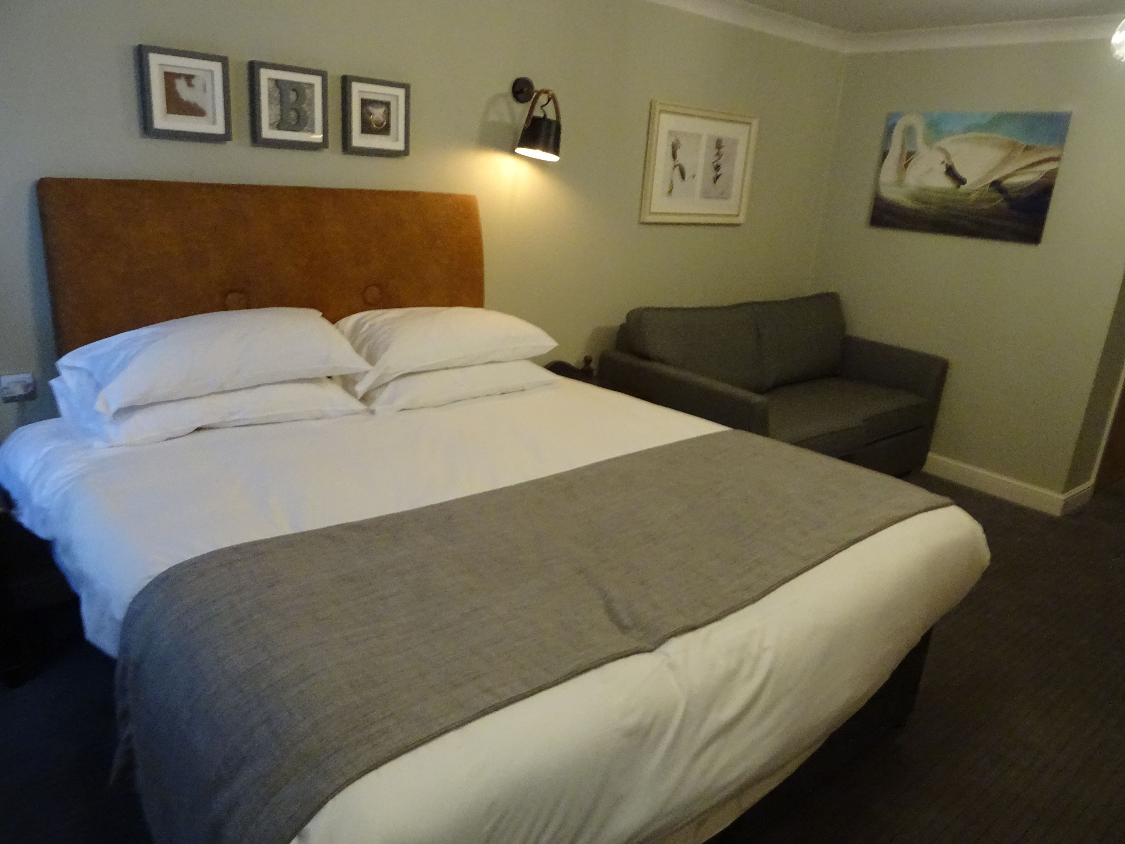 Een hotelkamer met een groot bed, een grijze bank en een schilderij aan de muur.