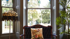 A bay window with stained glass, a chessboard, and a plush blue sofa with a floral pillow. - Belmore (Sale)