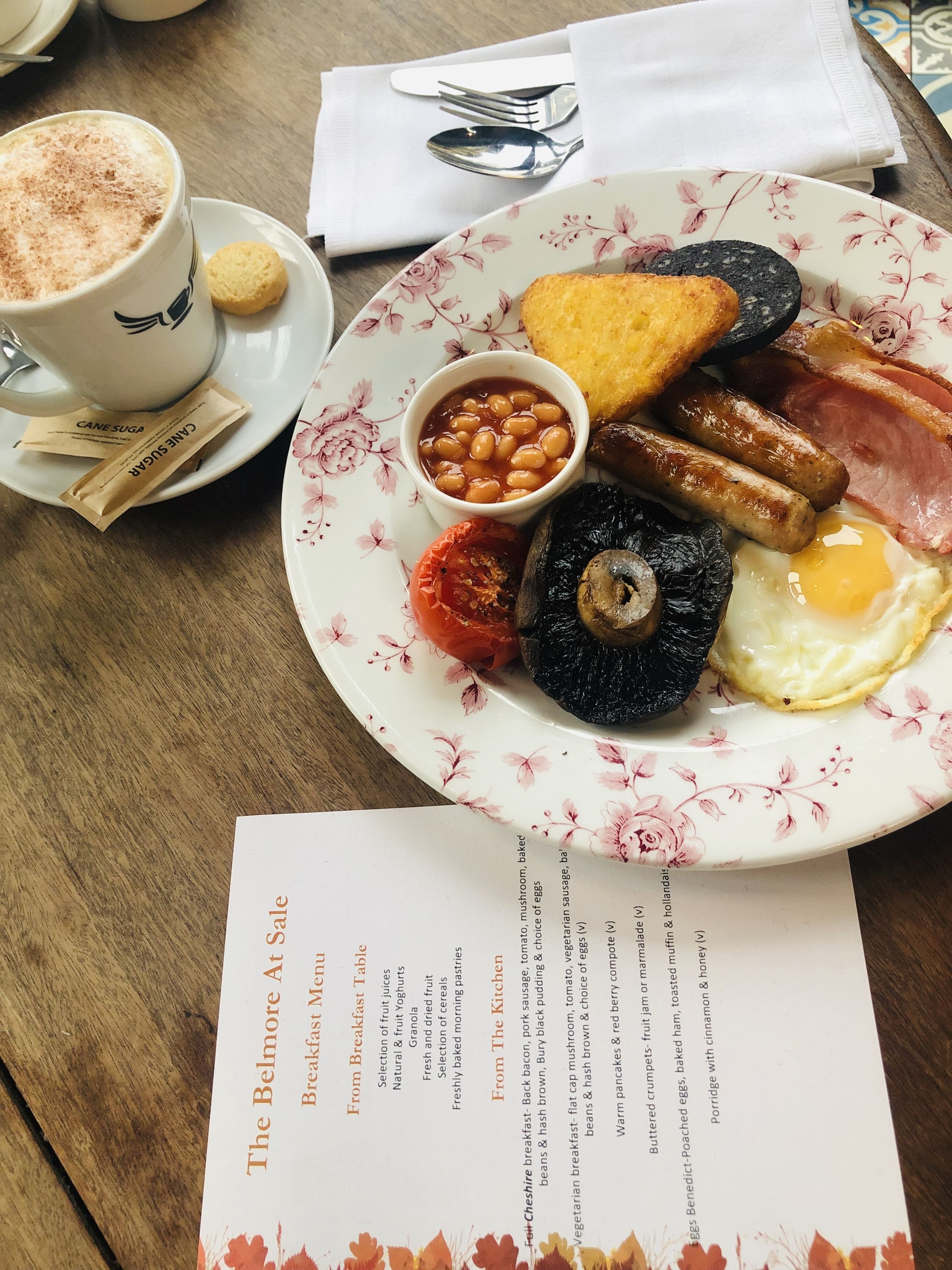 A breakfast plate with eggs, sausages, tomatoes, mushrooms, and toast, along with a cup of coffee and a menu.