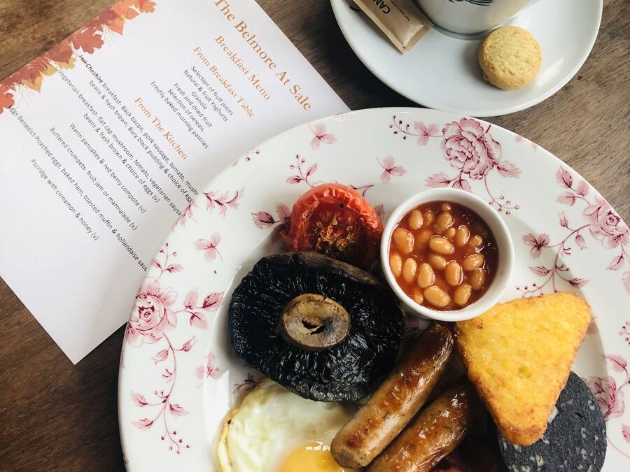 A breakfast plate with eggs, sausages, beans, and toast, a cup of coffee, and a menu.