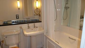 Une salle de bain avec un lavabo sur colonne, des toilettes et une baignoire équipée d’un pommeau de douche.