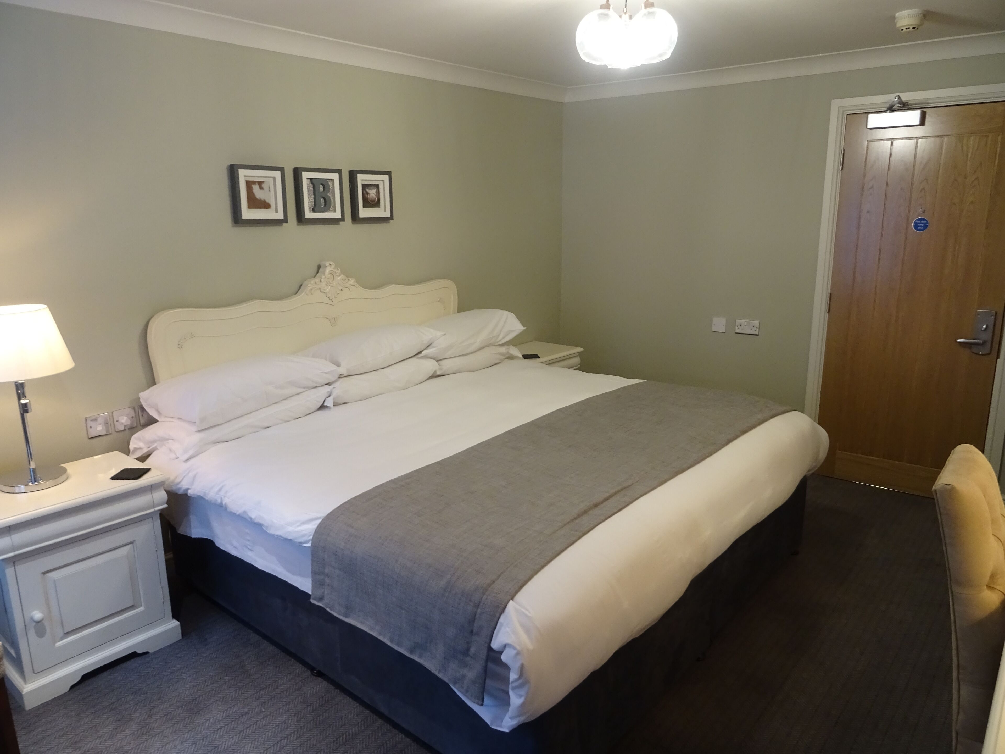 A neatly made bed with white linens, a bedside lamp, and a nightstand. There are three framed pictures on the wall above the bed.