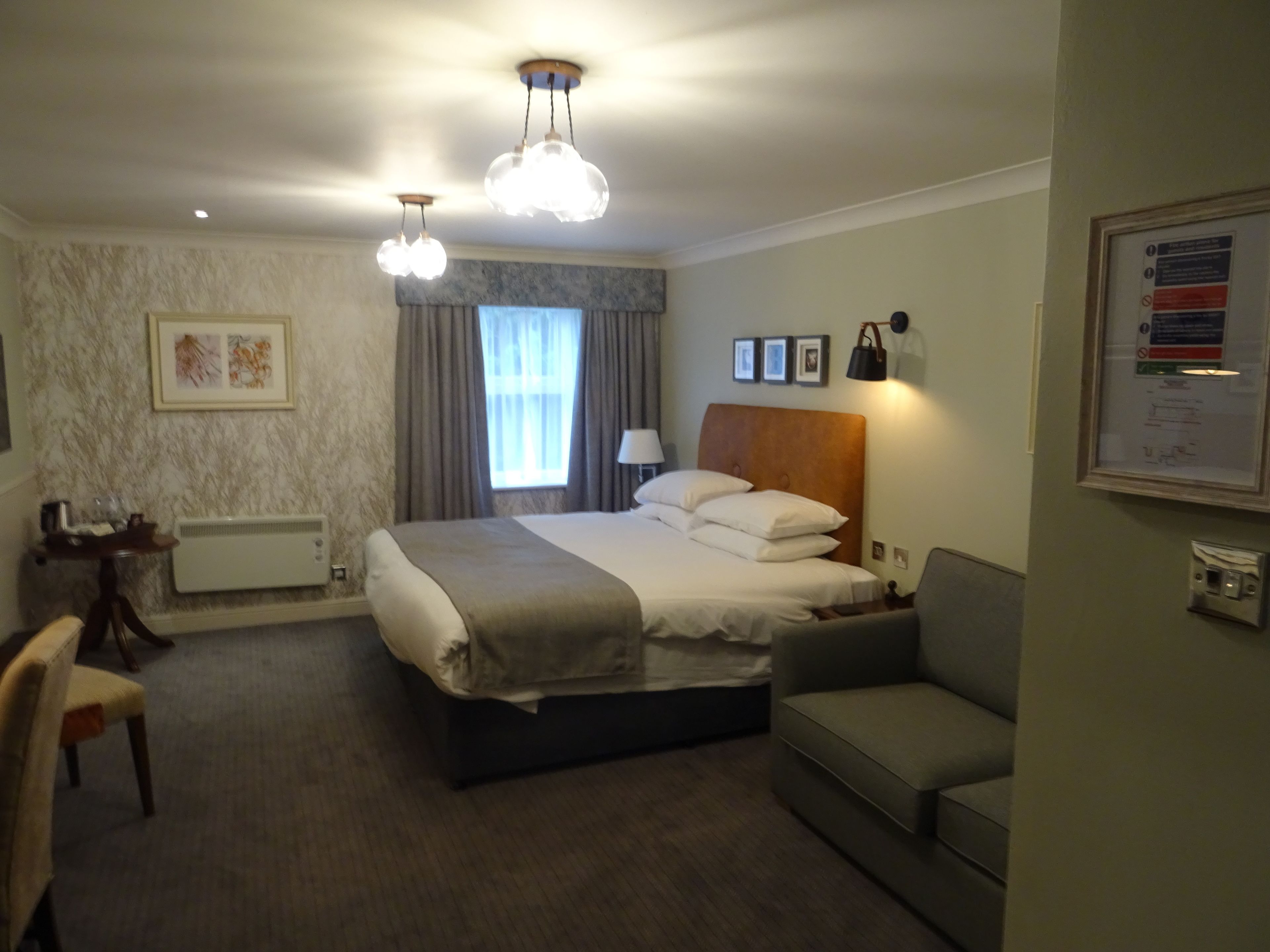 Ein Hotelzimmer mit Bett, Schreibtisch, Stuhl, einer Couch und einem Fenster mit Vorhängen.