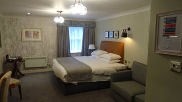 Ein Hotelzimmer mit Bett, Schreibtisch, Stuhl, einer Couch und einem Fenster mit Vorhängen.