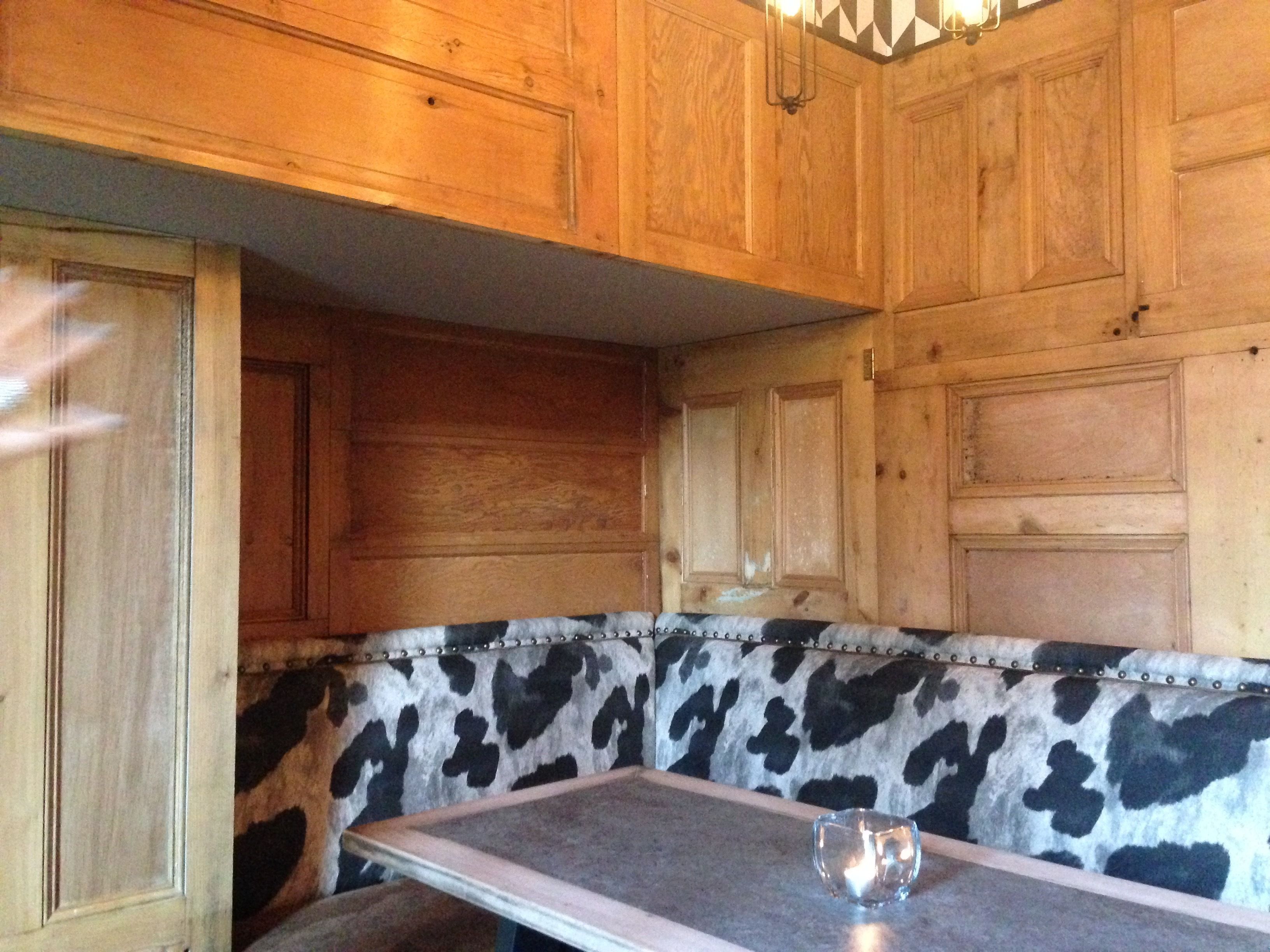 A wooden interior with a cowhide-patterned bench, wooden paneling, and a small table with a glass object on it.