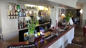A bar area with a variety of liquor bottles, a cash register, and a menu board. - Bell House Hotel & Restaurant (Chippenham)