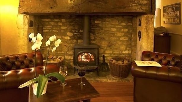 A cozy room with a stone fireplace, leather sofas, and a table with a vase and wine glasses. - Bell House Hotel & Restaurant (Chippenham)