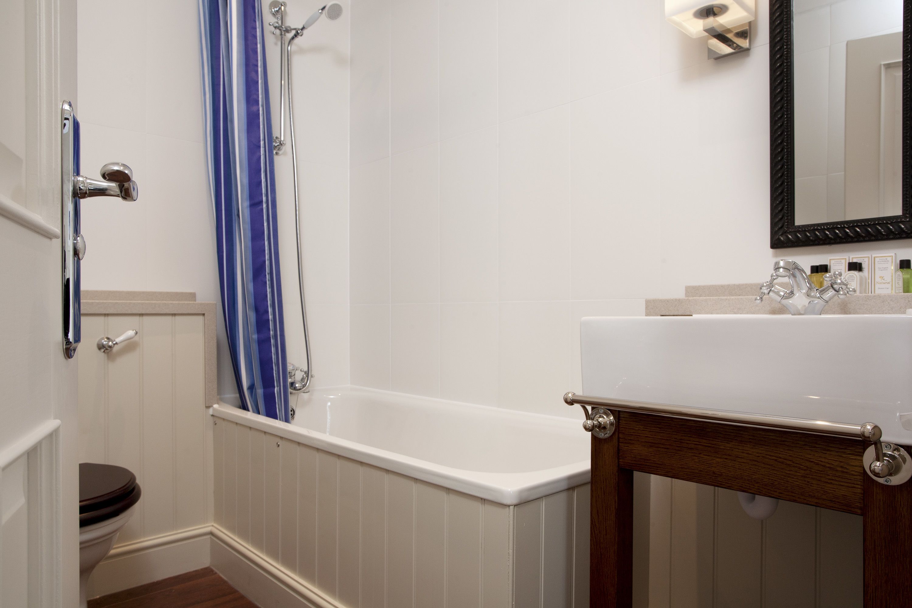 A bathroom with a white bathtub, a wooden vanity, a mirror, and a shower with a blue curtain.