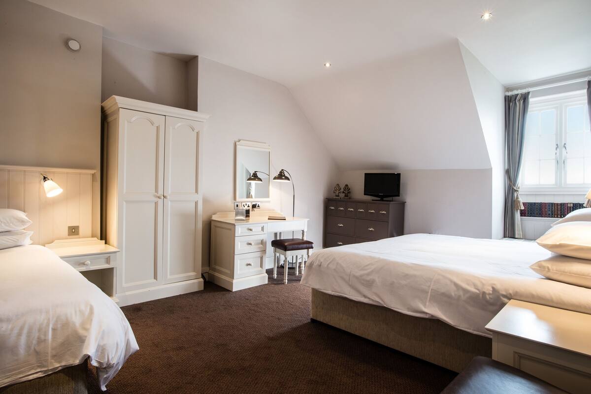 A bedroom with a large bed, a dresser, a vanity, and a television.