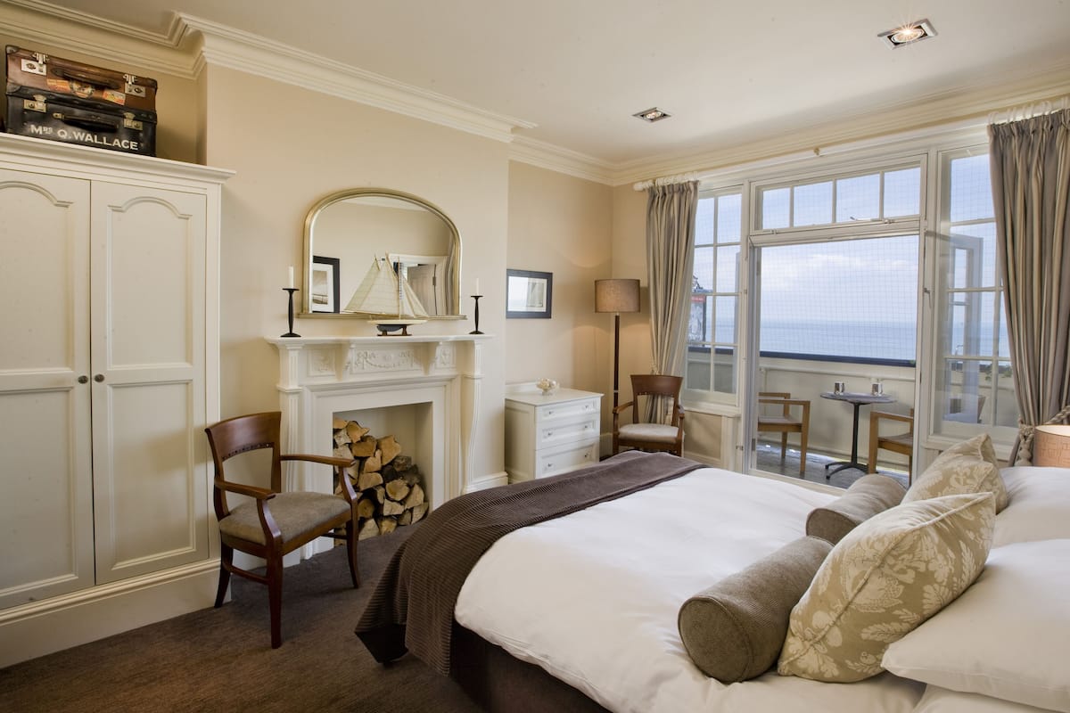A bedroom with a large bed, a fireplace, a desk, and a view of the sea.