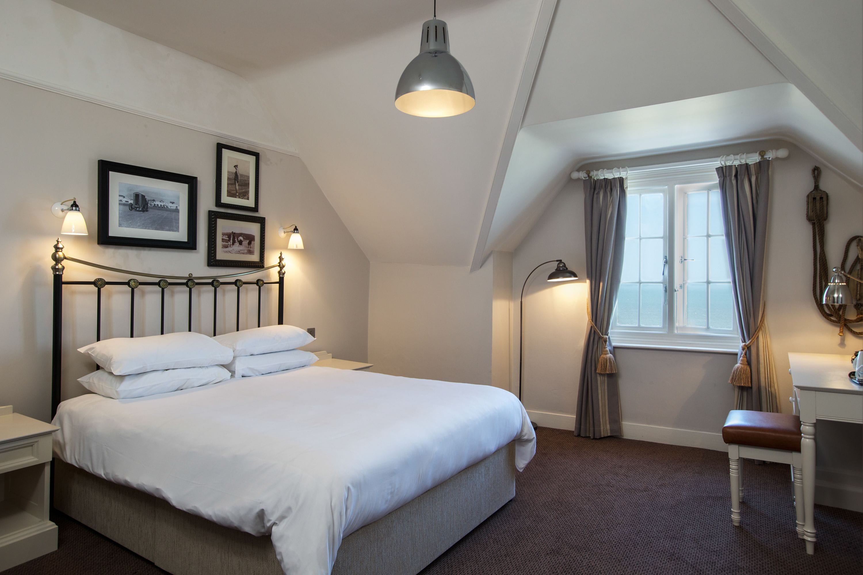 A neatly arranged bedroom with a large bed, bedside lamps, a desk, and a window with curtains.