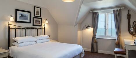 A neatly arranged bedroom with a large bed, bedside lamps, a desk, and a window with curtains.