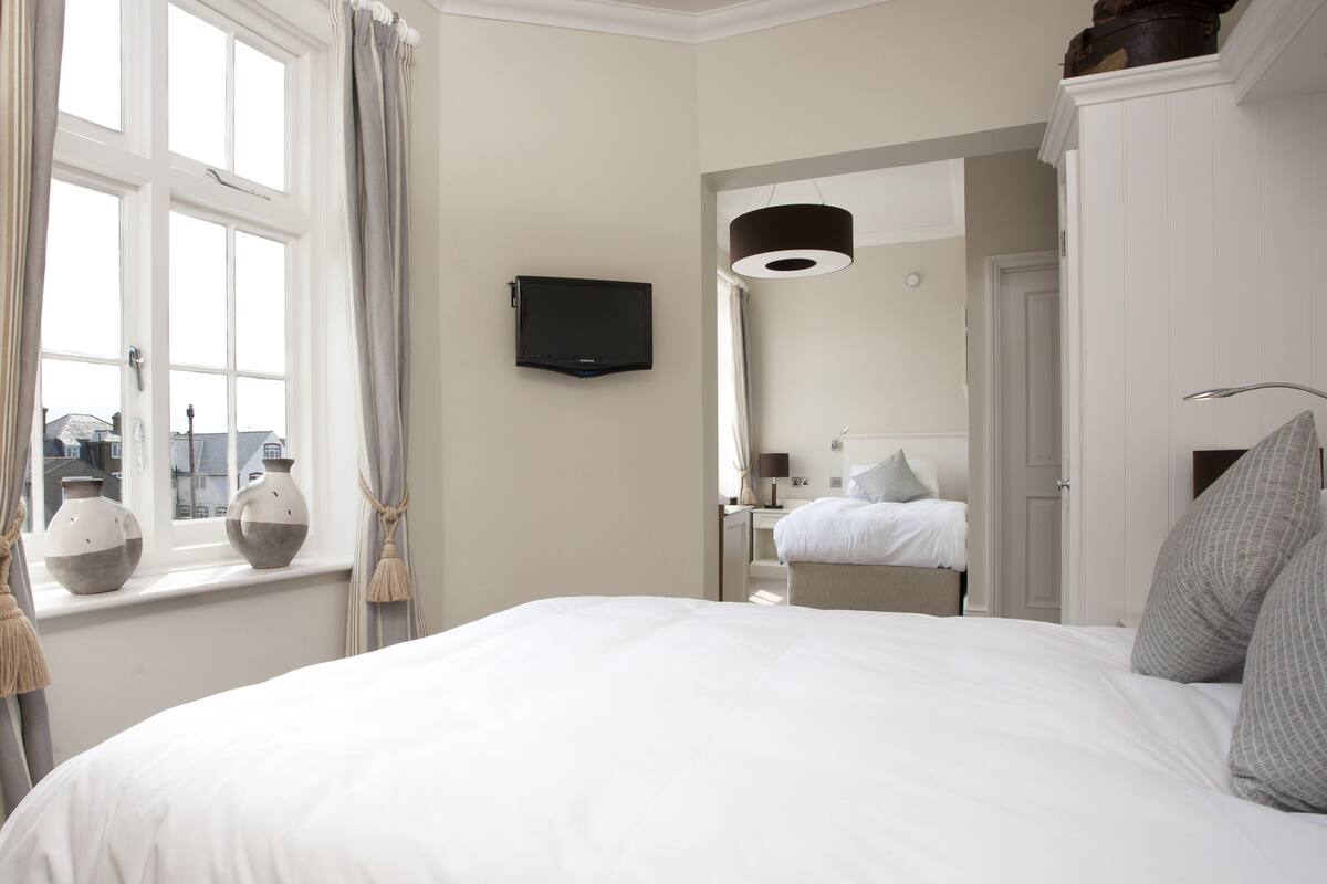 A hotel room with a large bed, a television mounted on the wall, a window with curtains, and a view of the city.